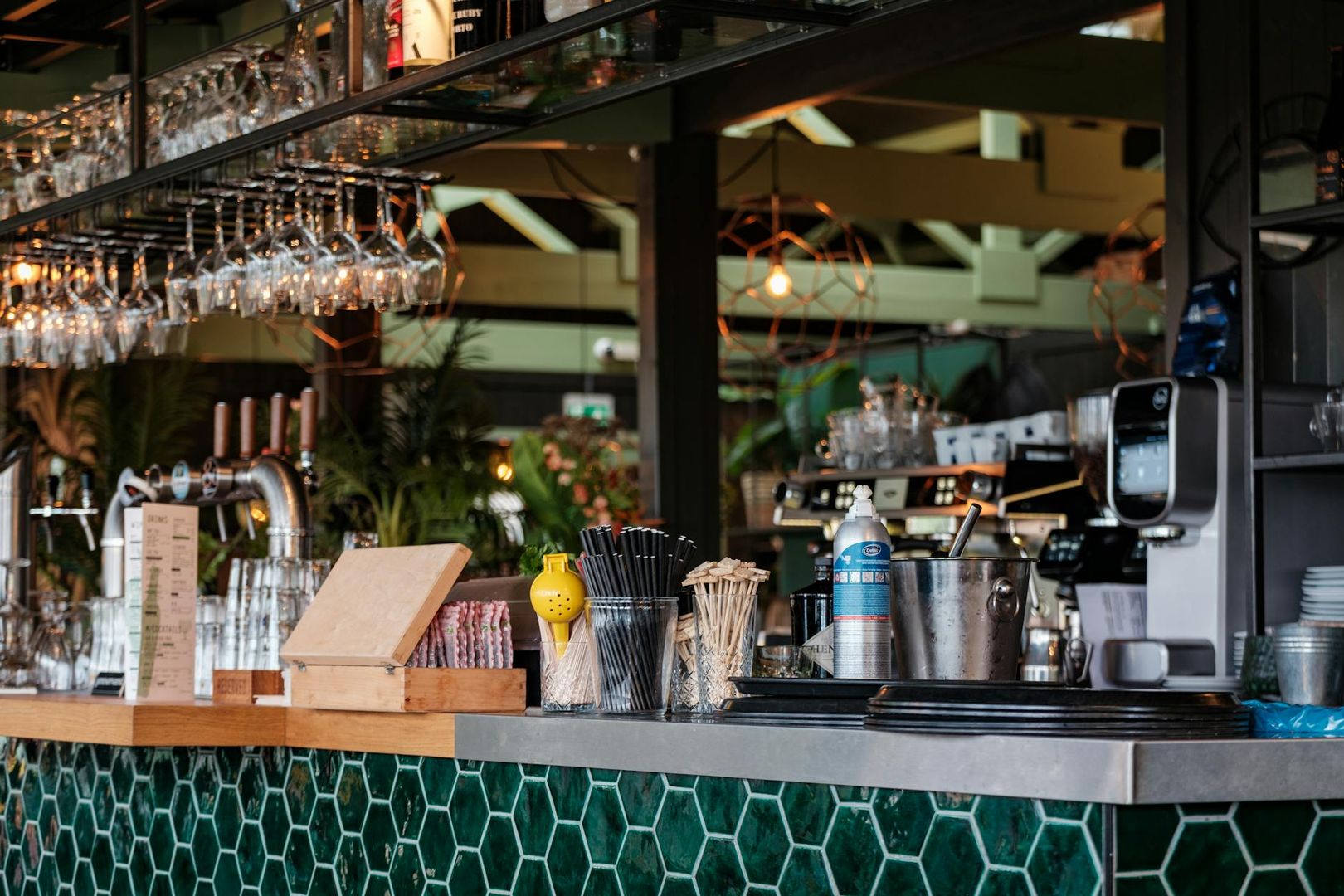 Välutrustad bardisk på ett modernt café med kaffemaskin och serveringstillbehör.