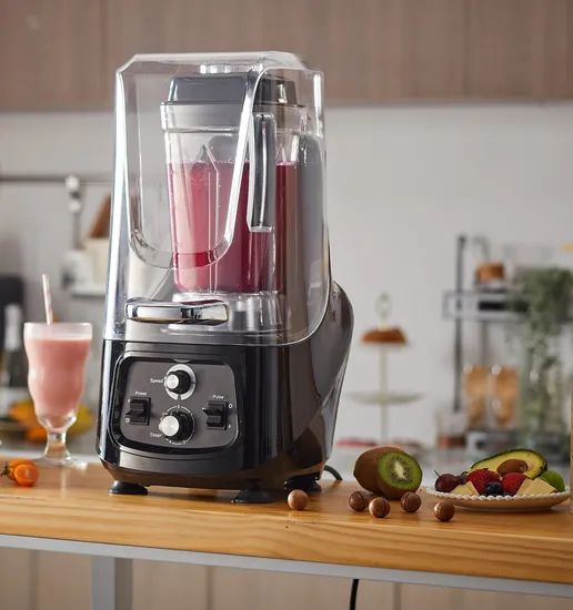 En professionell smoothie-blender med ljudhuv på en bänk med frukt.